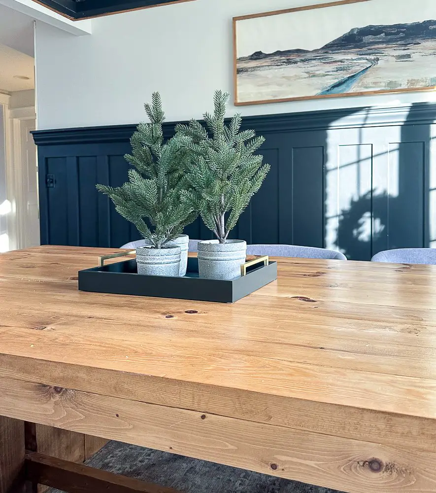 A dining table with 3 small Christmas trees on a tray in the center.