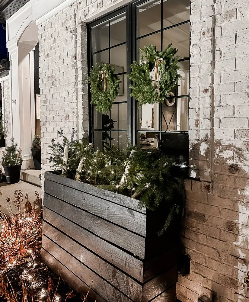 Black planter with boughs and birch logs. Twinkle lights too for a modern holiday home tour 2023.