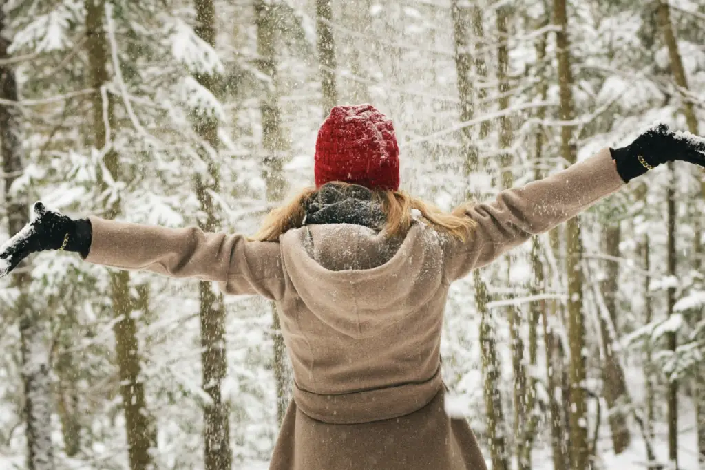 Girl standing in the snow with arms stretched out and dressed warm.