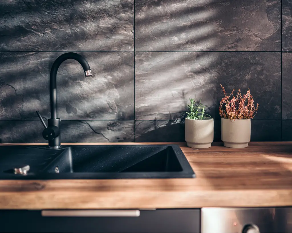 Kitchen sink with a black tile wall behind it.