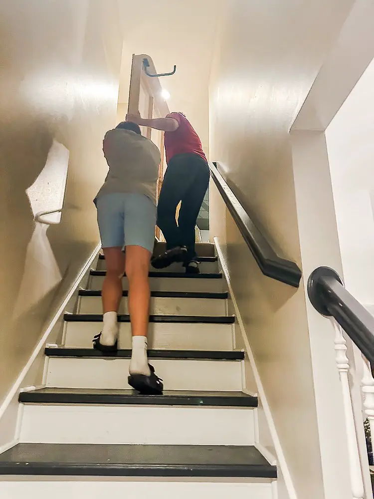 2 men carrying a bed frame up stairs for Murphy Bed Benefits post.
