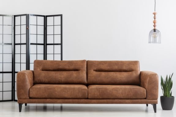 Leather furniture advantages: Leather sofa in a white living room with a window shade behind it.