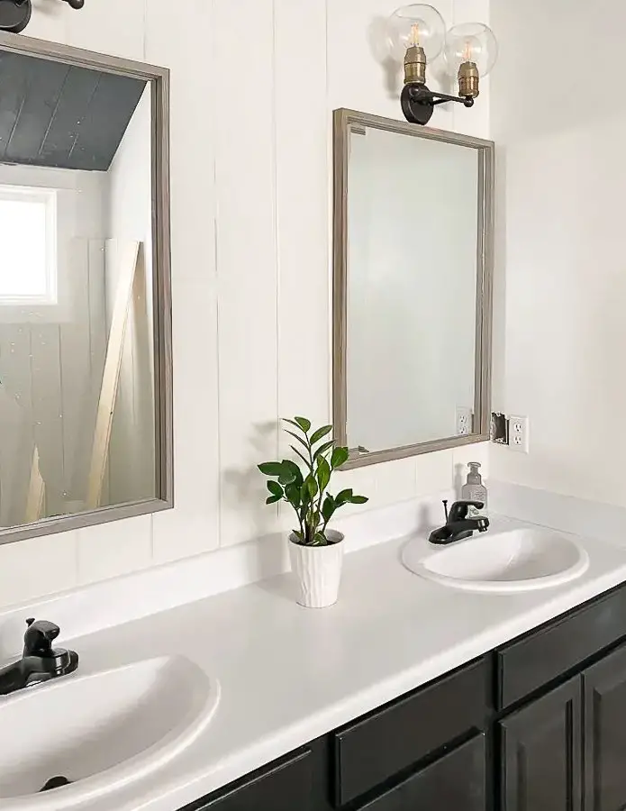 White countertops with 2 white sinks, 2 mirrors, black shelf.
