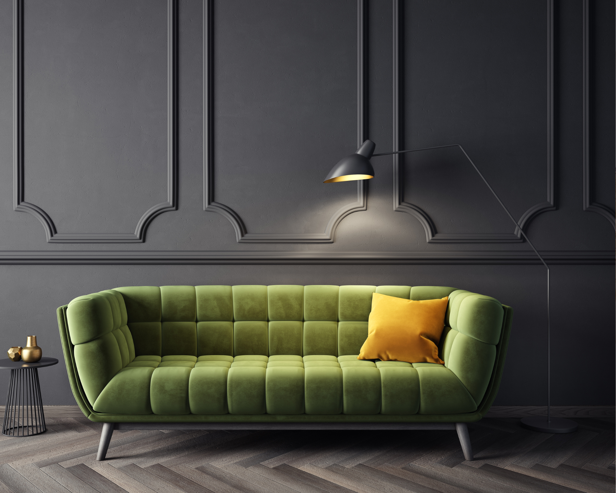 Picture frame moulding on a dark moody wall. Green sofa with yellow pillow in front of the wall.